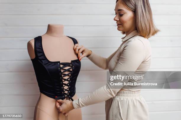 talented female tailor adds finishing touches to black corset with meticulously arranged black ribbons - corset stock pictures, royalty-free photos & images