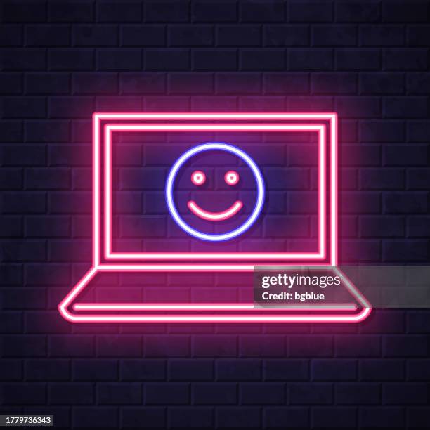 laptop with happy emoji. glowing neon icon on brick wall background - computer glow on face stock illustrations