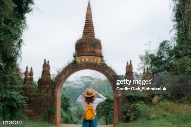 frau mit strohhut geht in der nähe des tores, das zu einem alten tempel im dschungel thailands führt - kambodschanische kultur stock-fotos und bilder