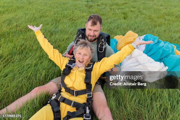 senior woman celebrating her first tandem parachute jump with her instructor - safety equipment stock pictures, royalty-free photos & images