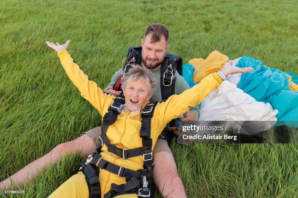 Senior woman celebrating her first tandem parachute jump with her instructor