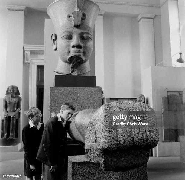 Two boys viewing the colossal granite head and arm of King Amenhotep III in the Egyptian Galleries of the British Museum, London, May 1954.