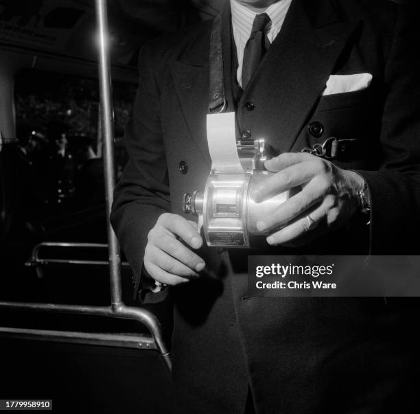 Close-up of a bus conductor issuing a ticket from a handheld ticket machine, London, April 1954.