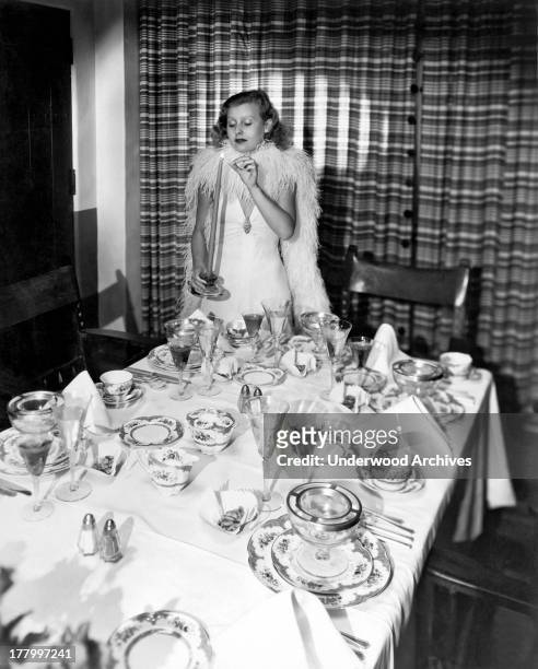 British actress Lillian Harvey lights a candle to finish off a table setting for a dinner party, Hollywood, California, c. 1933.