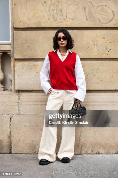 Maria Shindo wears cream toweling trousers, red knit tank top, white shirt, Miu Miu bag, gold necklace and brown sunglasses during the Womenswear...