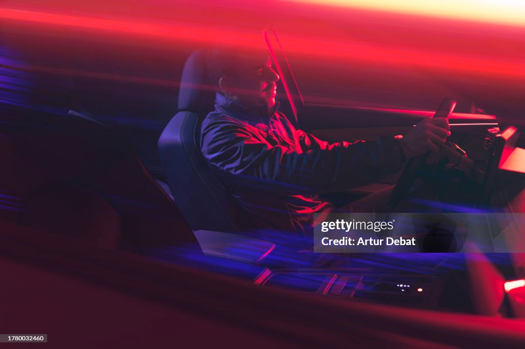 Happy man driving a car at night with red light trails in motion.