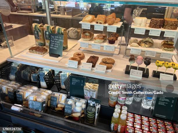 Various food items visible in display case at Starbucks including sandwiches, desserts, and beverages, products labeled with nutritional information...