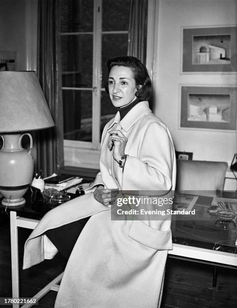 British industrial and interior designer Gaby Schreiber seated on the edge of her desk, May 15th 1958.