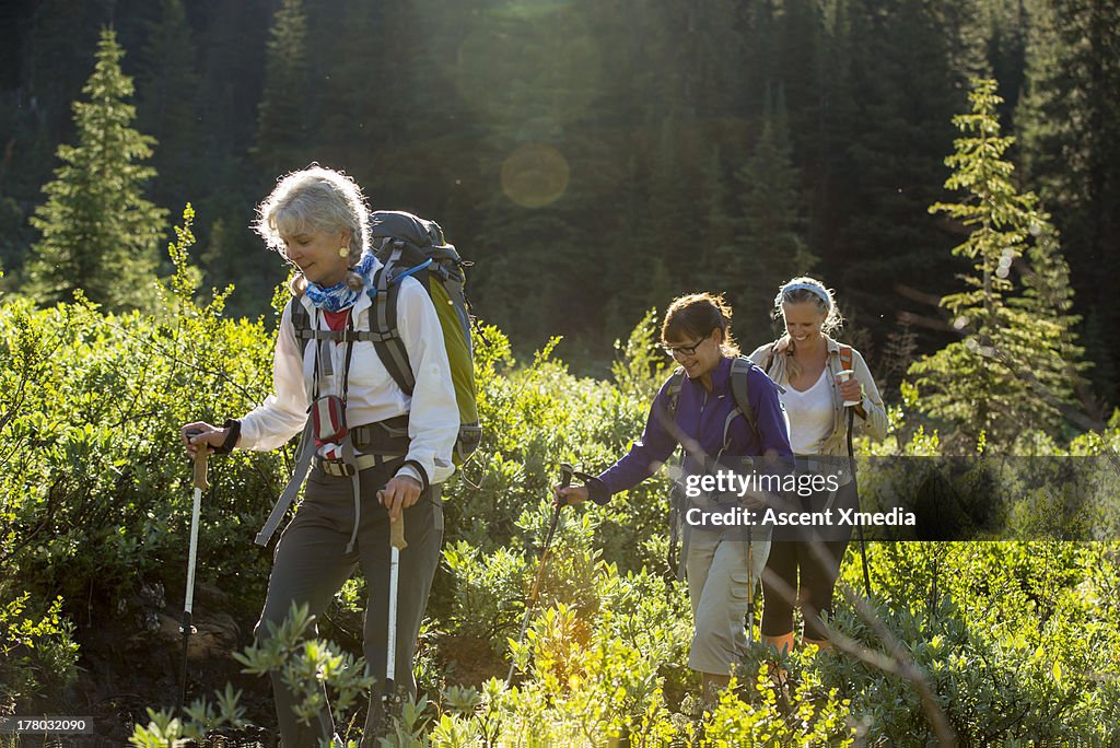 Three women hike through mountain meadow