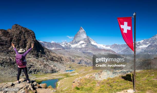 aufgeregte wandererin mit ausgestreckten armen vor freude am blick auf den riffelsee und das matterhorn - schweizer flagge stock-fotos und bilder