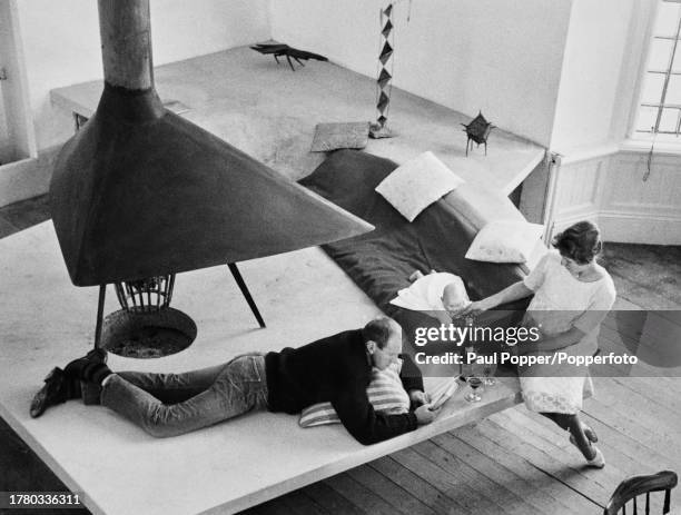 British artist and sculptor Lynn Chadwick lying on his front as his wife, Frances plays with their daughter Sarah near the large open fire Chadwick...