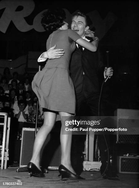 British singer and actor Adam Faith is embraced by schoolgirl Pandora Morcas as he performs on stage at the Royal Albert Hall in Kensington, London,...