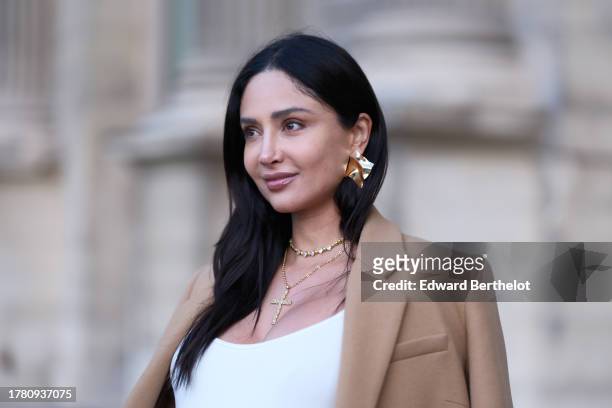 Patricia Gloria Contreras wears golden earrings, a golden necklace with cross detail, a beige winter coat, a white low-neck jumpsuit, during a street...