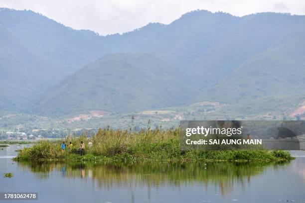 This photo taken on October 17, 2023 shows people standing on a floating island on Inle Lake in southern Shan State. Floating farms have become as...