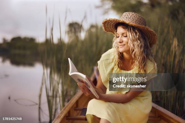 donna sorridente che gode mentre legge un libro in barca al fiume. - libri gialli estate foto e immagini stock