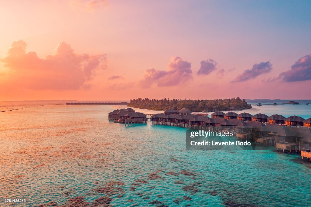 Amazing aerial beach landscape. Beautiful Maldives sunset seascape view. Horizon colorful sea sky clouds over water villa pier pathway. Tranquil drone view island lagoon tourism travel exotic vacation