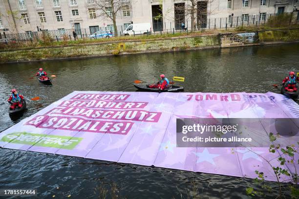 November 2023, Berlin: "Peace requires climate protection and social issues!" reads the banner that activists from Greenpeace are launching onto the...