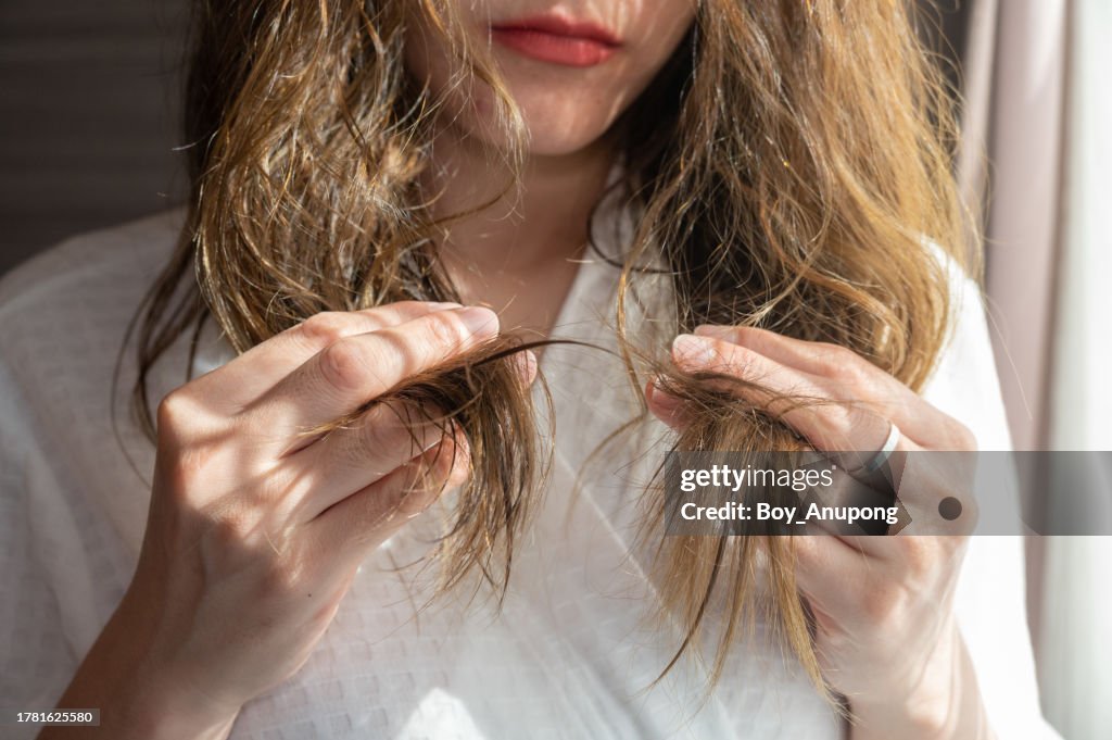 Cropped shot view of Asian woman holding her damaged split ended and messy hair.
