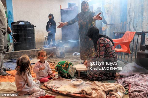 Woman reacts while another prepares traditional unleavened bread on an open fire at school run by the United Nations Relief and Works Agency for...