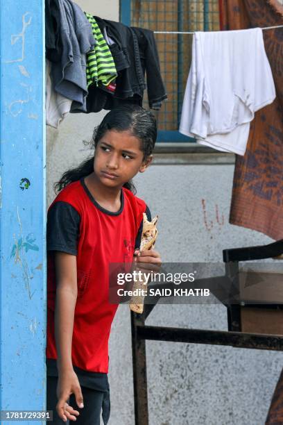 Girl holds a sandwich wrap as she stands behind laundry drying on a line at a school run by the United Nations Relief and Works Agency for Palestine...