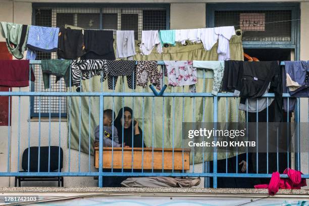 Woman speaks on a phone while carrying a child by drying laundry outside a classroom at a school run by the United Nations Relief and Works Agency...