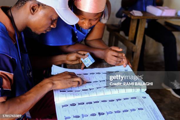 Polling station officials compare a voter's ID document to information on the voter's roll at a polling station in Monrovia on November 14, 2023....