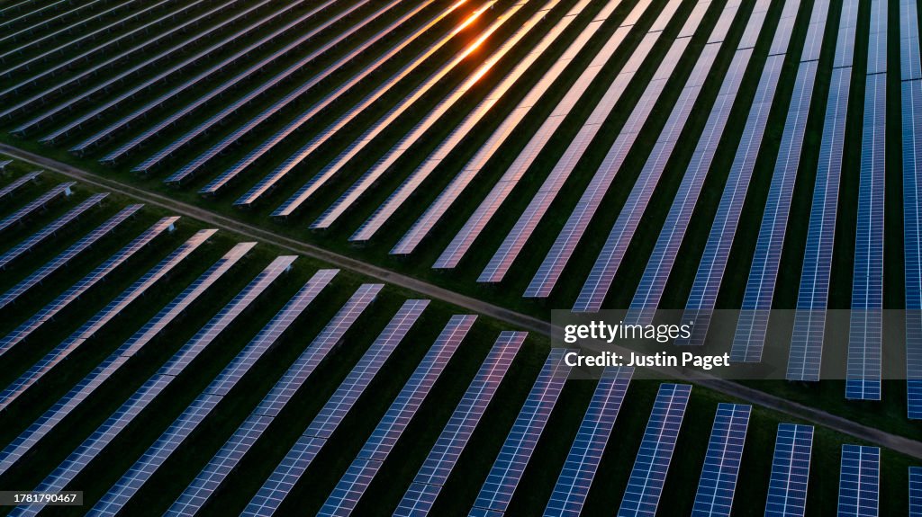 Drone view over a field of solar panels at sunset