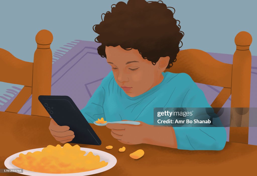 Messy, distracted boy eating macaroni and cheese and using smart phone at dining table
