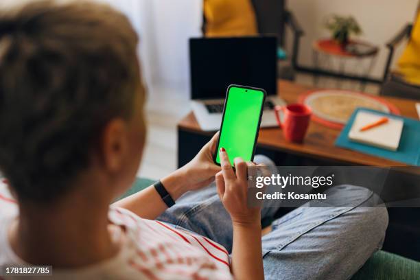 blick über die schulter einer frau, die ein mobiltelefon benutzt, während sie ihre finanzen von zu hause aus verwaltet - person surrounded by computer screens stock-fotos und bilder