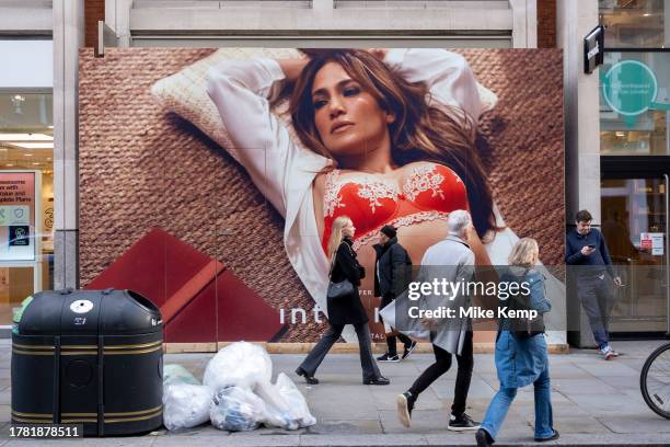 Shoppers and visitors out in Covent Garden pass a large scale hoarding featuring a photograph of American singer and actress Jennifer Lopez covering...