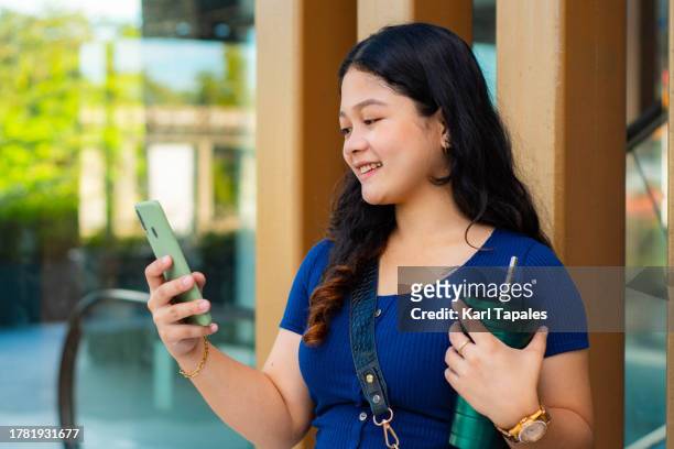 a portrait of a young southeast asian woman with digital devices outdoors during daytime - philippines stockfoto's en -beelden