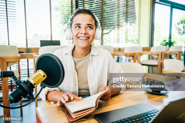 young smiling woman in white headphones sitting in front of laptop and microphone and recording podcast. - table of content stock pictures, royalty-free photos & images