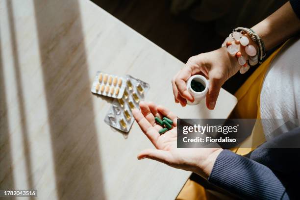 a woman standing at a table with green pills in her hand - hrt pill - fotografias e filmes do acervo