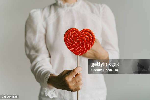 red heart shaped lollipop      

 in a woman's hand on a white background - lollipops stock pictures, royalty-free photos & images