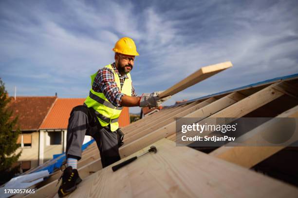 caucasian male roofer, working on a roof beam on a construction site - dakdekker stockfoto's en -beelden