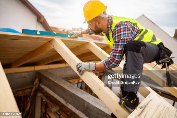 caucasian male roofer, using level while working on a roof beam on a construction site - trabalhador da construção civil imagens e fotografias de stock