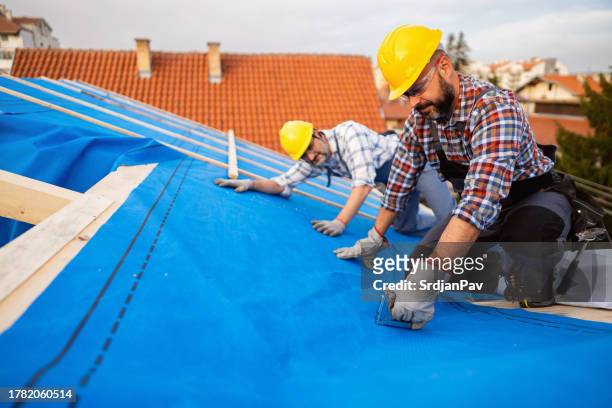 male caucasian roofers, placing an vapor permeable foil for an roof hydro isolation - roof inspector stock pictures, royalty-free photos & images
