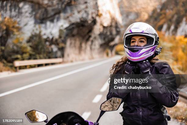 beautiful female biker puts crash helmet - female biker stock pictures, royalty-free photos & images