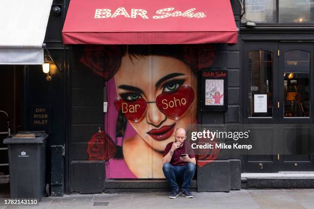 Man looking ta his smartphone has a cigarette break outside Bar Soho on 13th November 2023 in London, United Kingdom. Soho is an area of the City of...