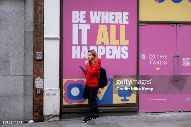 Young woman on her smartphone outside an available retail space at The Yards in Covent Garden on 13th November 2023 in London, United Kingdom. Things...