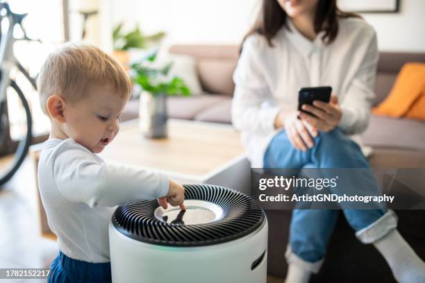 mother and her little boy adjusting air purifier at home. - air purifier stock pictures, royalty-free photos & images