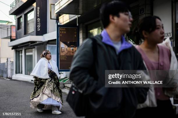 Couple walks in front of a woman wearing a traditional hanbok dress in Seoul on November 14, 2023.