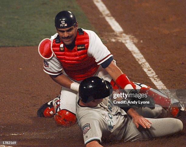 Jeff Conine of the Florida Marlins slides safely into home past catcher Eddie Perez of the Atlanta Braves during the first inning of game one of the...