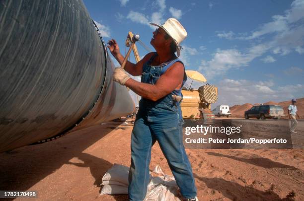 An expatriate American worker from Bechtel Corporation works together with local workers to join up pipe sections during construction of the...
