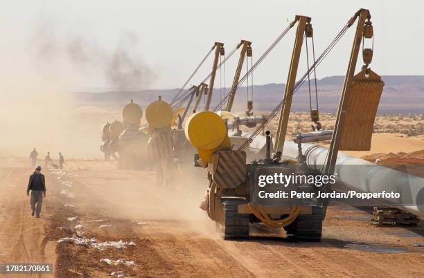 Construction workers use tracked bulldozers to hoist and bury a section of pipework during construction of the Maghreb-Europe Gas Pipeline in the...