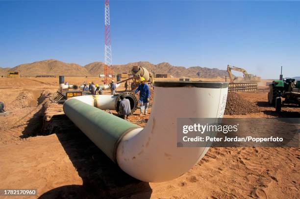 Construction workers, some wearing Bechtel Corporation hard hats, work on sections of pipework during construction of the Maghreb-Europe Gas Pipeline...