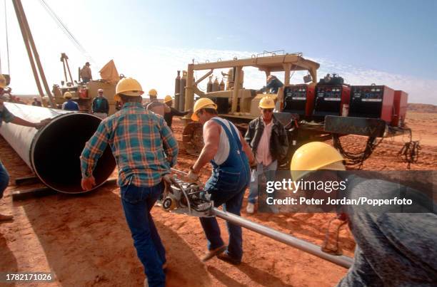 Expatriate American workers from Bechtel Corporation work together with local workers to join up pipe sections during construction of the...