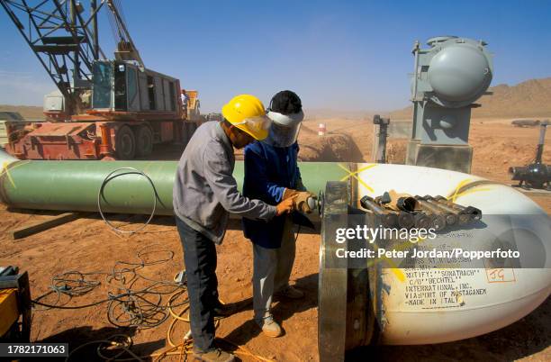 Construction workers, one wearing a Bechtel Corporation hard hat, work on sections of pipework during construction of the Maghreb-Europe Gas Pipeline...