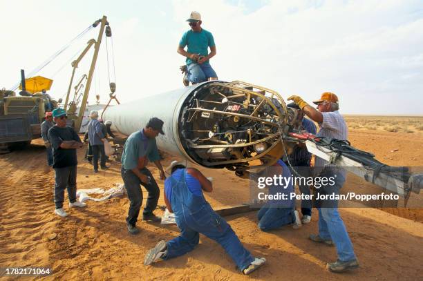 Expatriate American workers from Bechtel Corporation work together with local workers to join up pipe sections during construction of the...