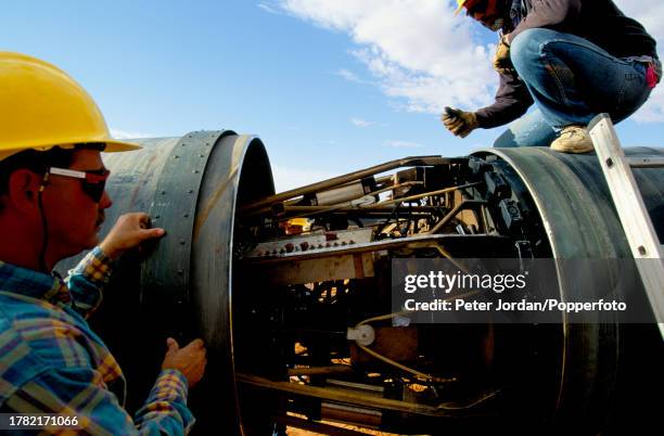 Expatriate American workers from Bechtel Corporation work together with local workers to join up pipe sections during construction of the...